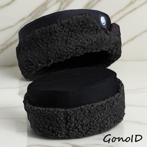 May include: Two black winter hats with a round crown and a fluffy, dark grey trim. The hats are made of a soft material and have a small logo on the side. The hats are displayed on a white marble surface.