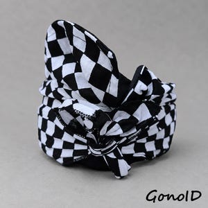May include: A black and white chequered fabric headband featuring a knotted bow detail at the centre. The textile has a repeating square pattern throughout, and the word GonolD is printed in black in the lower right corner of the image.