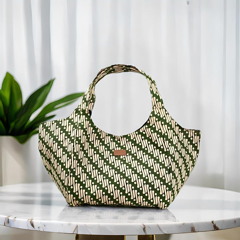 Peut inclure: Sac fourre-tout vert et blanc &agrave; motifs avec une poign&eacute;e incurv&eacute;e. Le sac pr&eacute;sente un motif diagonal r&eacute;p&eacute;t&eacute; de points et de lignes blancs sur un fond vert fonc&eacute;. Une petite &eacute;tiquette rectangulaire marron est cousue sur le devant.