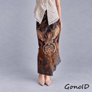 Könnte beinhalten: Ein langer, gerade geschnittener Rock mit schwarzer Basis und komplexen Batikmustern in Braun, Orange und Creme. Der Rock wird mit einem ärmellosen, weißen Oberteil mit Lochstickerei kombiniert. Der Text "GonolD" steht unten rechts im Bild.