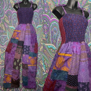 May include: A patchwork jumpsuit in shades of purple, featuring a smocked bodice and wide-leg pants. The jumpsuit has adjustable tie straps and is displayed on a black mannequin. The patchwork design incorporates various patterns and textures.