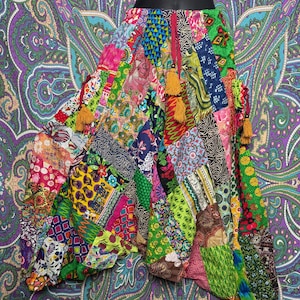 Puede incluir: Una falda patchwork con una vibrante mezcla de colores y patrones. La falda está hecha de varias piezas de tela, incluyendo diseños florales y geométricos. Tiene un estilo bohemio fluido, con borlas en el dobladillo.