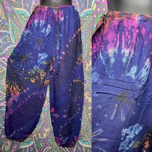 May include: Tie-dye pants in shades of blue, purple, pink, and orange. The pants have a drawstring waist and a relaxed fit. The tie-dye pattern radiates from the center of the pants. The fabric appears to be lightweight.