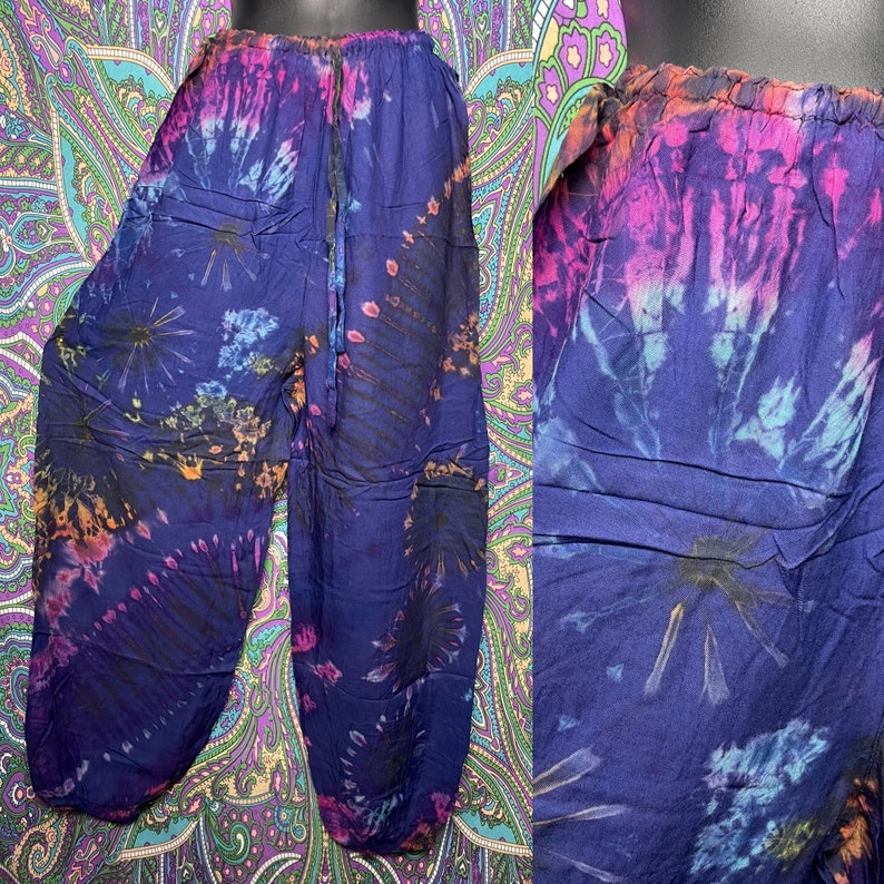 May include: Tie-dye pants in shades of blue, purple, pink, and orange. The pants have a drawstring waist and a relaxed fit. The tie-dye pattern radiates from the center of the pants. The fabric appears to be lightweight.