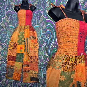 以下が含まれることがあります： オレンジ、赤、緑の色合いのパッチワークジャンプスーツ。トップスは結び紐付きで、パンツには様々な模様のパッチが付いています。ジャンプスーツは黒いマネキンに展示されています。