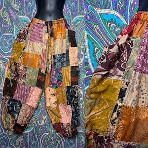 May include: Patchwork trousers featuring a variety of fabric squares in shades of mustard yellow, deep red, dark brown, and muted purple. The pants have an elasticized waistband with a drawstring and a loose, relaxed fit with tapered leg openings.