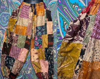 May include: Patchwork trousers featuring a variety of rectangular fabric segments in shades of mustard yellow, deep burgundy, dark brown, and muted teal. The garment has an elasticized waistband with a drawstring and loose-fitting legs.
