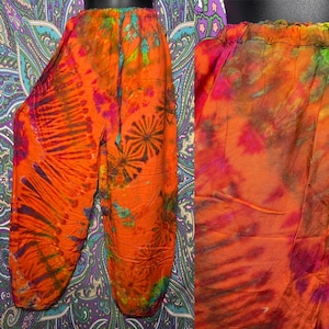 May include: Orange tie-dye pants with a drawstring waist. The pants feature a vibrant pattern of orange, pink, and green hues. The design includes radial and floral-like patterns. The pants are made of a lightweight fabric.