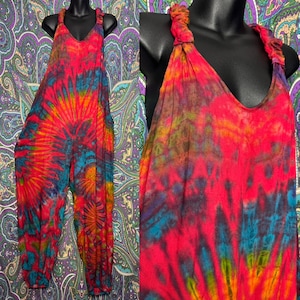 Può includere: Una tuta senza maniche con un vivace motivo tie-dye nei toni del rosso brillante, arancione, giallo e blu. Il capo presenta uno scollo a V, spalline arricciate e gambe ampie che si restringono alle caviglie con polsini elasticizzati.