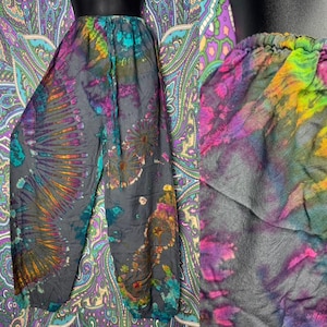 May include: Tie-dye pants in shades of gray, teal, purple, and orange. The pants have an elastic waistband and a loose, flowing fit. The tie-dye pattern features a radial design on the legs and floral-like patterns.