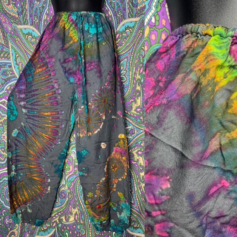 May include: Tie-dye pants in shades of gray, teal, purple, and orange. The pants have an elastic waistband and a loose, flowing fit. The tie-dye pattern features a radial design on the legs and floral-like patterns.