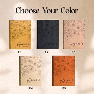 K&ouml;nnte beinhalten: Eine Auswahl personalisierter Rezeptb&uuml;cher in verschiedenen Farben, darunter Senfgelb, Schwarz und Pfirsich. Jedes Buch hat ein Blumendesign und den Namen "Agnes's" mit dem Text "Recipe Book". Der Satz "Choose Your Color" steht oben.