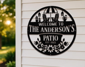 May include: Black metal patio sign with a circular design. The sign features the text "WELCOME TO THE ANDERSON'S PATIO EST. 2025". The design includes an umbrella, two chairs, hanging lanterns, and floral accents.