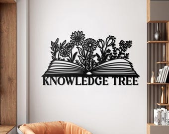 May include: Black metal wall art depicting an open book with flowers and foliage growing from it. The text "KNOWLEDGE TREE" is displayed below the book. The artwork is mounted on a white wall.