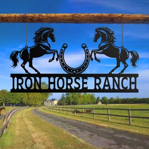 May include: Black metal sign with two rearing horse silhouettes flanking a horseshoe. The sign reads "IRON HORSE RANCH" in bold, cut-out letters. The sign hangs from a wooden beam against a blue sky.