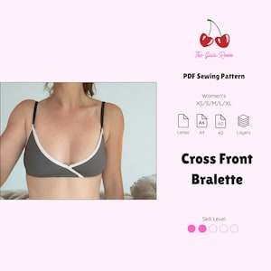 Op de afbeelding: Een grijze bralette met een witte kanten rand langs de halslijn en dunne zwarte bandjes. De tekst luidt: The Girls Room, PDF Sewing Pattern, Women's XS/S/M/L/XL, Letter, A4, A0, Layers, Cross Front Bralette, en Skill Level met bijbehorende iconen.