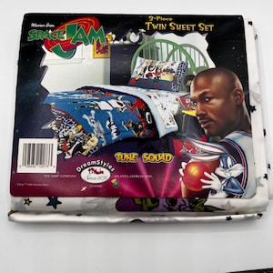 May include: A 3-piece twin sheet set featuring the Space Jam movie theme. The set includes a comforter and pillowcases with cartoon characters and the Tune Squad logo. The packaging shows Michael Jordan and Bugs Bunny.