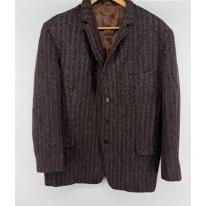 May include: A dark brown blazer featuring a vertical herringbone pattern, a notched lapel, and three front buttons. The garment includes two lower flap pockets, one chest pocket, and a smooth brown interior lining visible at the collar area.