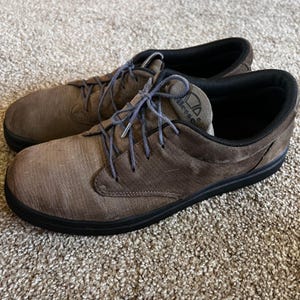 May include: A pair of brown suede casual shoes with black soles and laces. The shoes have a low-profile design and the brand name "ellesse" is visible on the tongue.