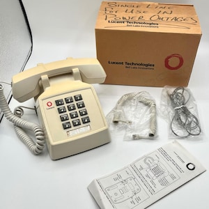 May include: A vintage beige Lucent Technologies telephone with a keypad, handset, and coiled cord. The phone is accompanied by a box labeled "SINGLE LINE FOR USE IN POWER OUTAGES." Additional accessories and a manual are also present.
