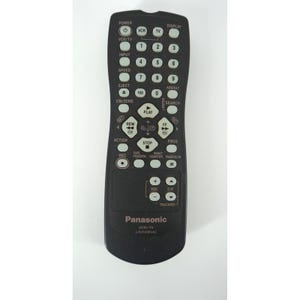 May include: A black Panasonic VCR/TV universal remote control with numerous buttons for power, input, speed, and playback functions. The remote has a curved bottom and includes volume and channel controls.