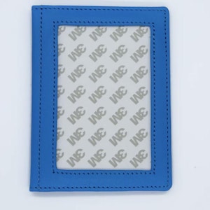 May include: A blue leather-like frame with a rectangular window. The frame has stitched edges and a white interior with the repeated text "3M". The frame is designed to hold a photo or document.