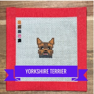 May include: A needlepoint canvas featuring a Yorkshire Terrier design. The dog is rendered in brown, tan, and black stitches, set against a white grid. The canvas has a red border, and a purple banner at the bottom reads "Yorkshire Terrier."