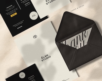 Może przedstawiać: Zestaw artykułów papierniczych, w tym wizytówki, kartka z podziękowaniami i koperta. Karty zawierają logo "ÉLAN STUDIO" w kolorze czarnym na białym tle. Czarna koperta zawiera napis "thank you" elegancką czcionką.
