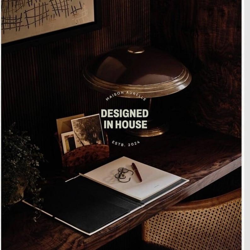 May include: A dark brown desk with a lamp, notepad, and stationery. The lamp has a brown shade and gold base. A notepad with a pen and a pair of glasses is on the desk. The text "MAISON AURELLE DESIGNED IN HOUSE ESTB. 2024" is visible.