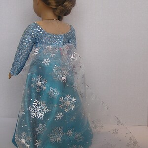 Puede incluir: Un vestido azul y plateado con estampado de copo de nieve y una superposici&oacute;n transparente. El vestido lo lleva una mu&ntilde;eca con el pelo casta&ntilde;o.