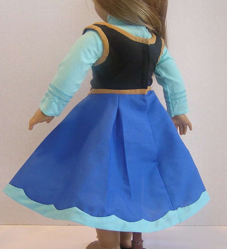 May include: A blue and light blue dress with a black vest and gold trim. The dress has a scalloped hemline.