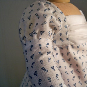 May include: A white dress with blue floral print and a white ruffle neckline. The dress has puffed sleeves and a fitted bodice.