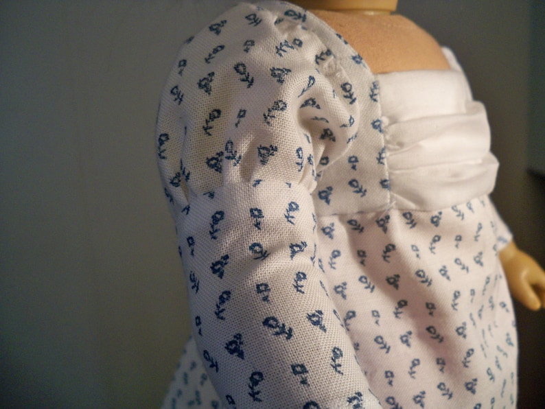 May include: A white dress with blue floral print and a white ruffle neckline. The dress has puffed sleeves and a fitted bodice.