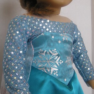 Puede incluir: Un vestido azul y plateado con un patr&oacute;n de copo de nieve. El vestido tiene un corpi&ntilde;o brillante y mangas largas.