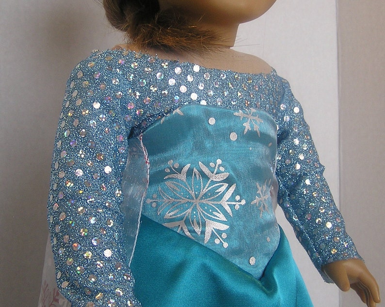 Puede incluir: Un vestido azul y plateado con un patr&oacute;n de copo de nieve. El vestido tiene un corpi&ntilde;o brillante y mangas largas.