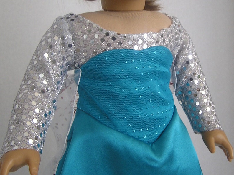 Puede incluir: Un vestido azul turquesa con mangas de lentejuelas plateadas. El vestido tiene un corpi&ntilde;o ajustado y una falda fluida.