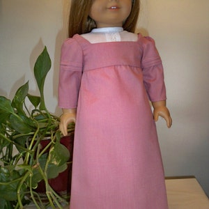 May include: A pink dress with a white collar and long sleeves. The dress is made of a soft, textured fabric and has a simple, elegant design.