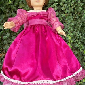 Puede incluir: Un vestido de mu&ntilde;eca de sat&eacute;n rosa con ribete de encaje blanco y mangas transparentes. El vestido tiene un corpi&ntilde;o ajustado y una falda completa.