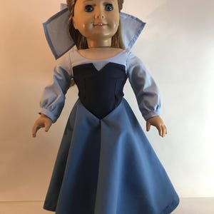 K&ouml;nnte beinhalten: Eine Puppe in einem hellblauen und marineblauen Kleid mit passendem Kragen. Die Puppe hat blondes Haar und blaue Augen. Das Kleid hat lange &Auml;rmel und einen weiten Rock. Die Puppe steht aufrecht.