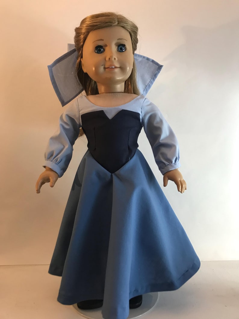 K&ouml;nnte beinhalten: Eine Puppe in einem hellblauen und marineblauen Kleid mit passendem Kragen. Die Puppe hat blondes Haar und blaue Augen. Das Kleid hat lange &Auml;rmel und einen weiten Rock. Die Puppe steht aufrecht.