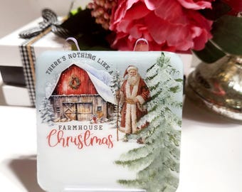 May include: A rectangular Christmas decoration depicting a winter scene with a red barn, Santa Claus, and a snow-covered evergreen tree. The text "THERE'S NOTHING LIKE A FARMHOUSE Christmas" is displayed in the image.