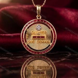 Op de afbeelding: Een goudkleurige hangerketting met een cirkelvormig ontwerp. De hanger heeft een centraal met diamanten bezet kruis en de Franse tekst "QU HIER QUE DEMAIN". De buitenste ring is bekleed met rode edelstenen.