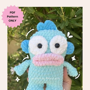 May include: A handmade, light blue crochet Lil Sea Guy plushie with white eyes, a pink mouth, and blue accents. The text "PDF Pattern ONLY" is in a pink starburst, and "LIL SEA GUY PATTERN BY @KNOT.ELLIS" is at the bottom. The plushie is held in a hand.