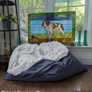 May include: A large blue pet bed with a white, fluffy top. The bed is shown in a room with a stained glass window featuring a dog. The text "Pictured: Size Large; Blue" is at the bottom.
