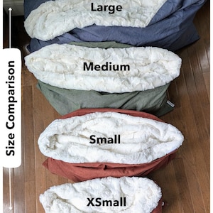 May include: A size comparison of four pet beds: Large, Medium, Small, and XSmall. Each bed has a plush, cream-colored interior and a different colored exterior: blue, green, rust, and a darker rust. The text "Size Comparison" is on the left.