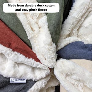 May include: Close-up of a patchwork blanket with various fabric textures and colors. The blanket features a plush white fleece border and is made from durable duck cotton. The text "Made from durable duck cotton and cozy plush fleece" is visible.