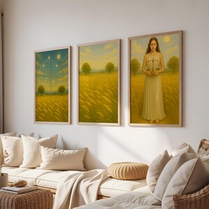May include: Set of three framed art prints. The artwork depicts a serene landscape with a golden field, trees, and a figure holding scales. The color palette includes shades of yellow, green, and blue, creating a calming atmosphere. The frames are light-colored wood.