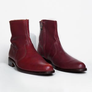 May include: A pair of burgundy leather ankle boots. The boots have a rounded toe, a low heel, and a side zip. The leather has a slight sheen, and the boots appear to be well-worn.