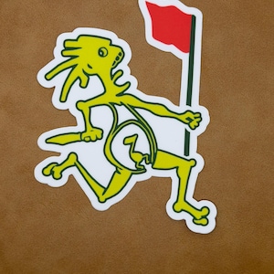 Peut inclure: Un autocollant découpé représentant un personnage de dessin animé jaune courant avec un drapeau rouge. La figurine a un contour blanc et est sur un fond marron. Le drapeau est sur un poteau vert et blanc.