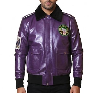Puede incluir: Una chaqueta de cuero púrpura con cuello y puños negros. La chaqueta tiene dos bolsillos delanteros y un parche en el pecho con un emblema verde y amarillo. Un parche más pequeño está en la manga izquierda.